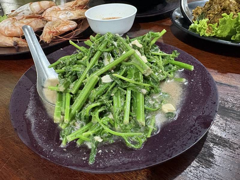 ผัดผักเขียวสดจานใหญ่ มีกุ้งเผาวางอยู่ด้านหลัง